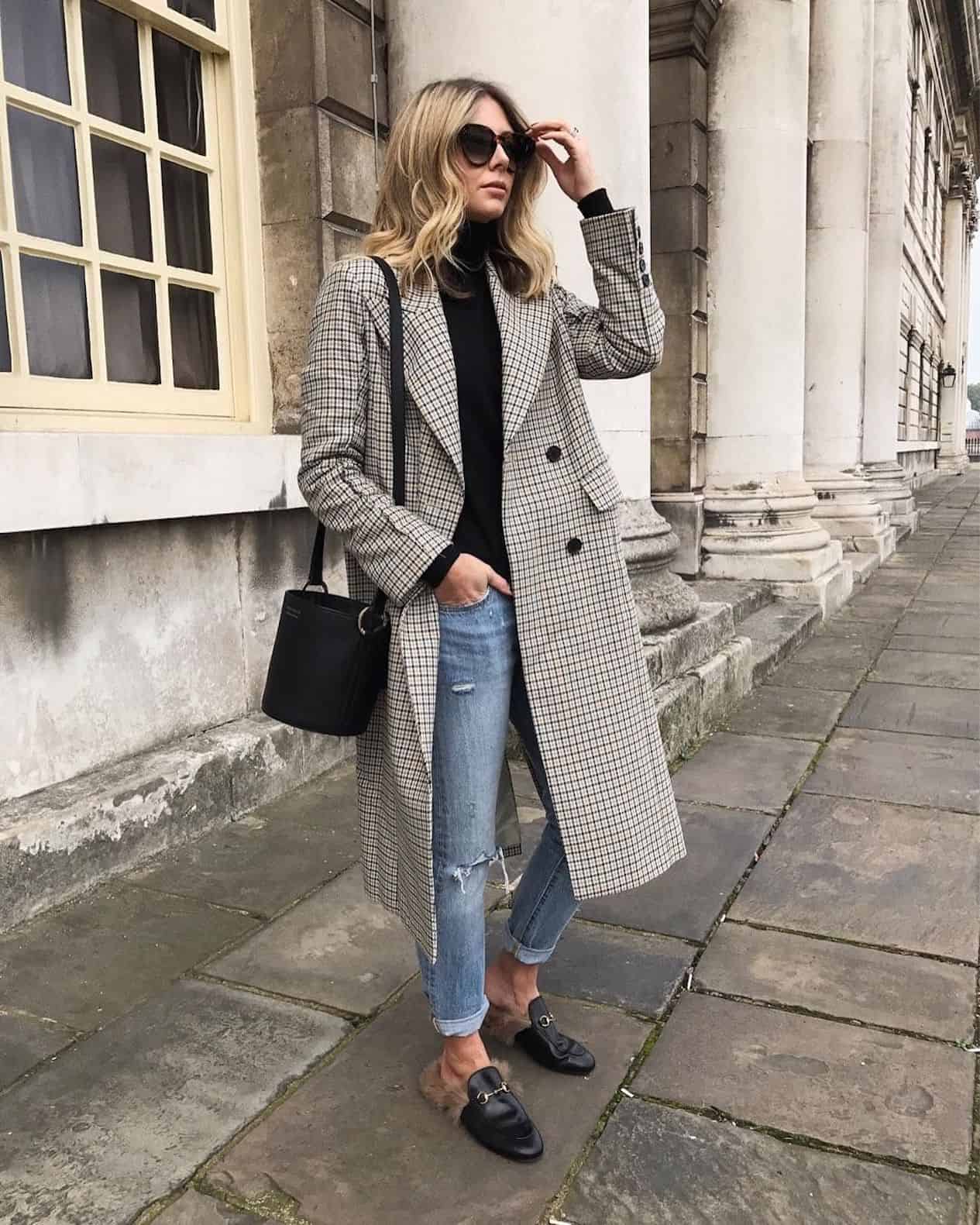 image of a woman standing on a sidewalk wearing a long grey trench coat, jeans, and a pair of Gucci mules