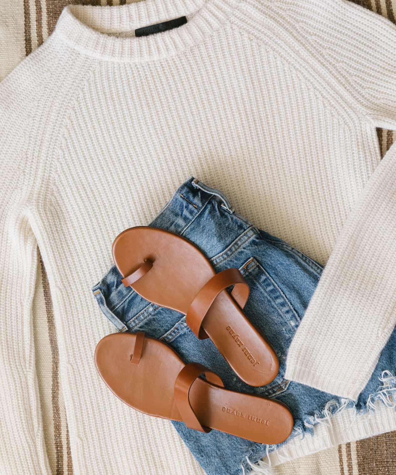 image of an outfit flatly with a knit cashmere fisherman sweater, blue denim shorts, and brown sandals
