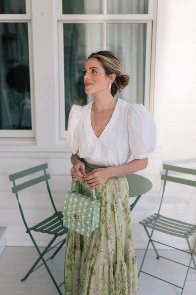 image of a woman standing on a porch wearing a white blouse and a floral midi skirt
