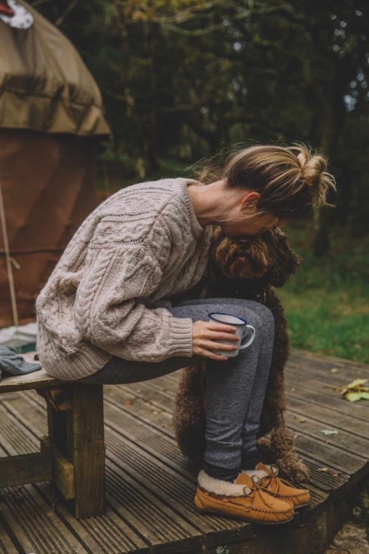 Girl wearing blue joggers, a cream sweater, and UGG moccasins near a camping site.