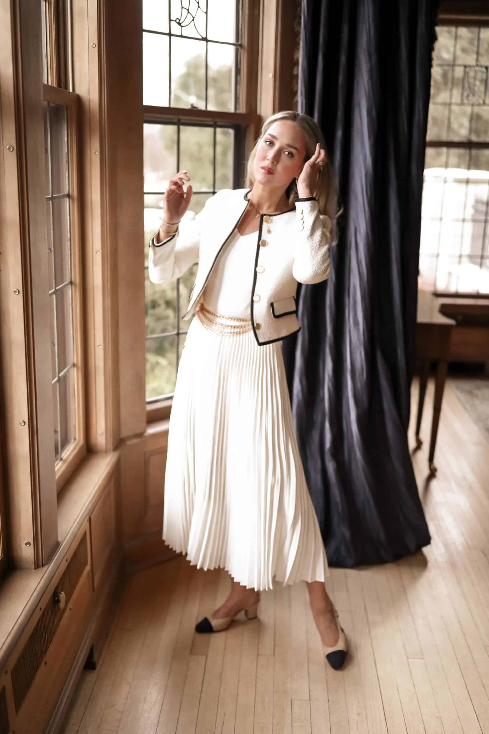 woman wearing a white tweed blazer, pleated ivory skirt, and chanel heels