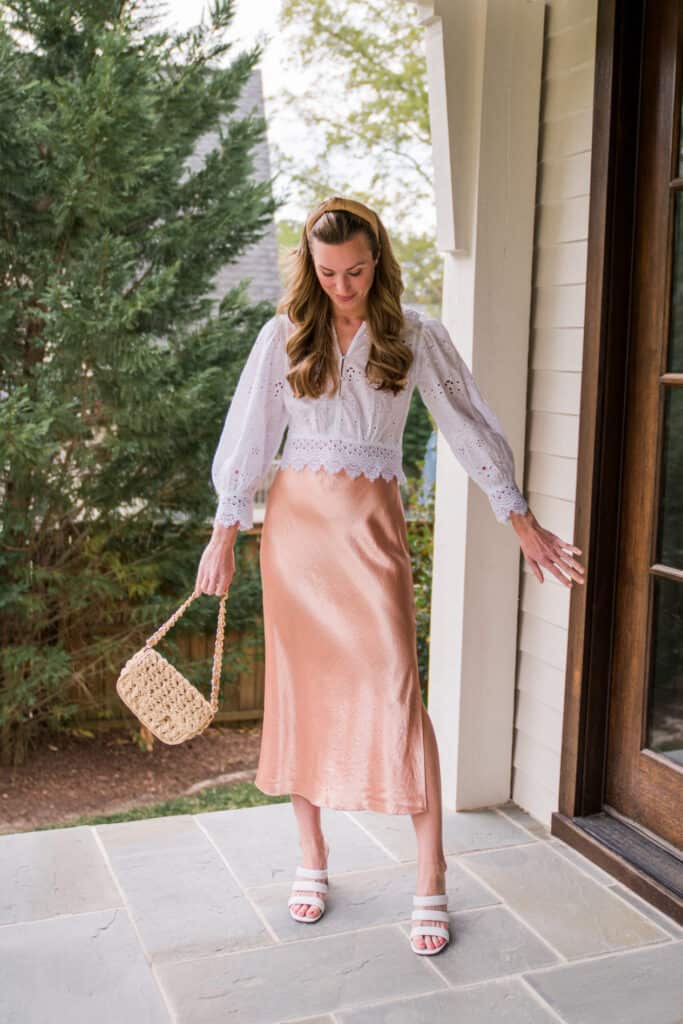 image of a woman standing on a porch wearing a white blouse and a pink silk midi skirt