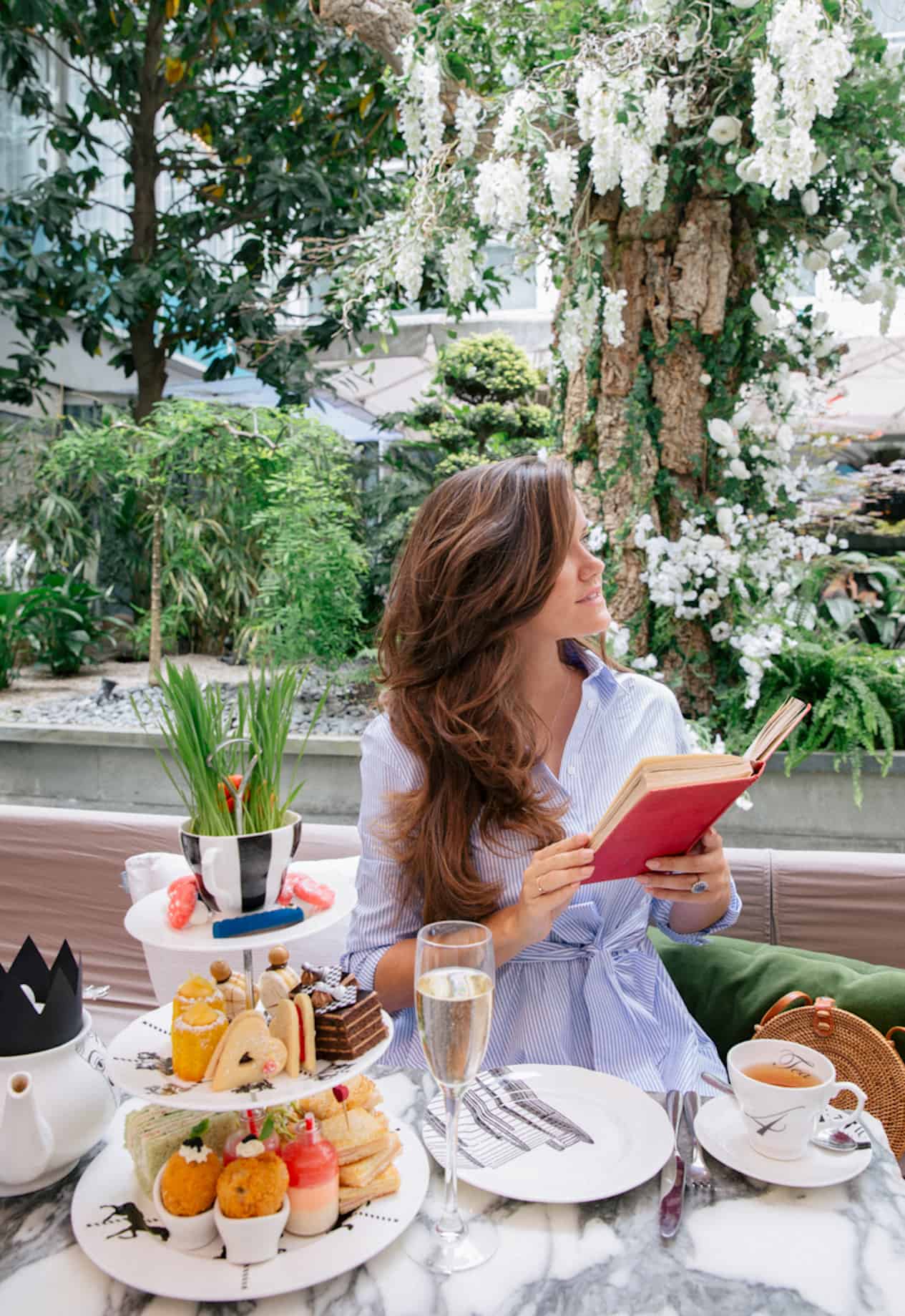 a woman in a blue striped dress sitting at a table enjoying high tea