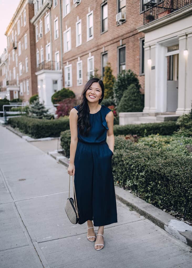 image of a woman standing on a sidewalk wearing a navy blue silk jumpsuit and heels