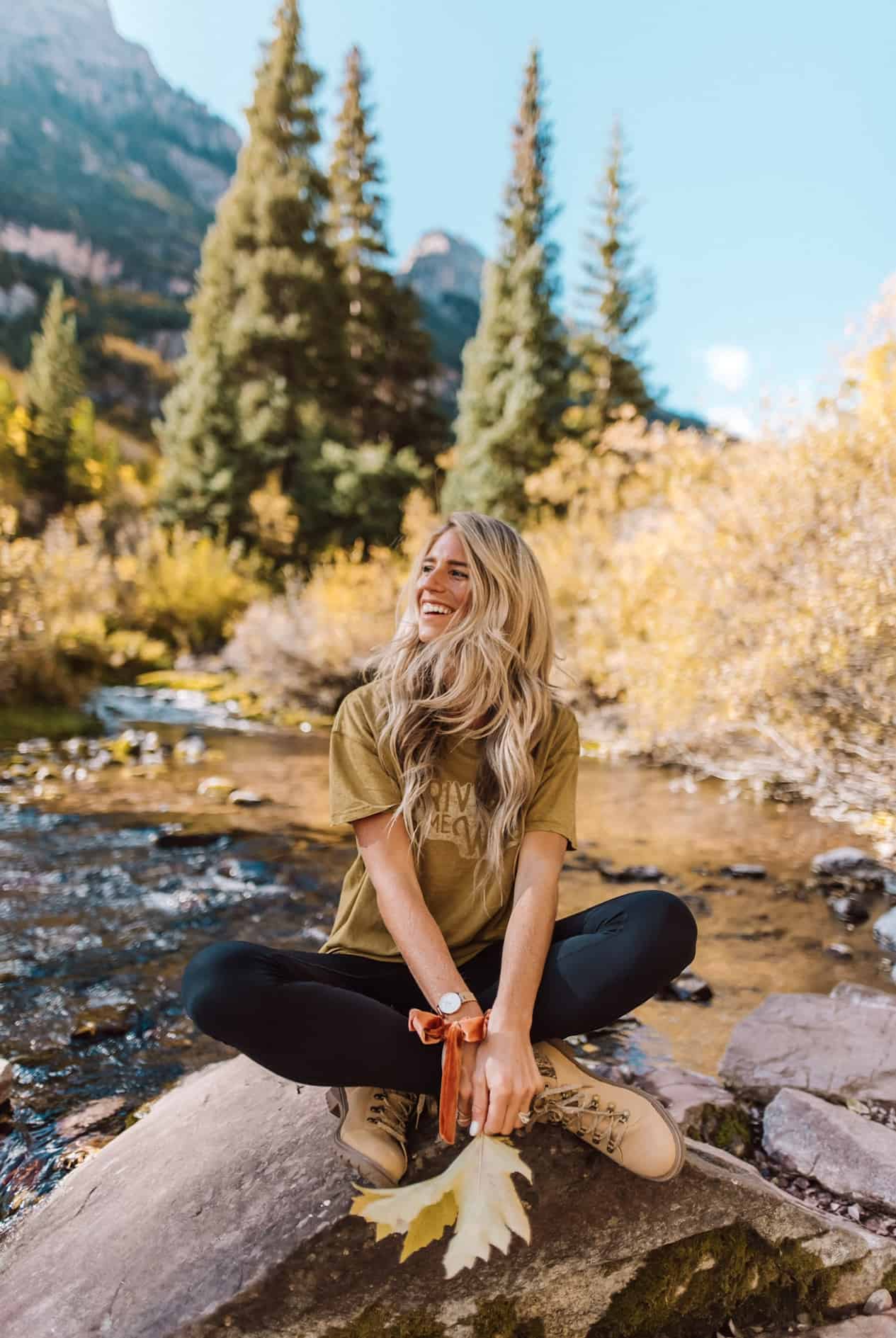 Girl near a river wearing black leggings, hiking boots, and a t-shirt.
