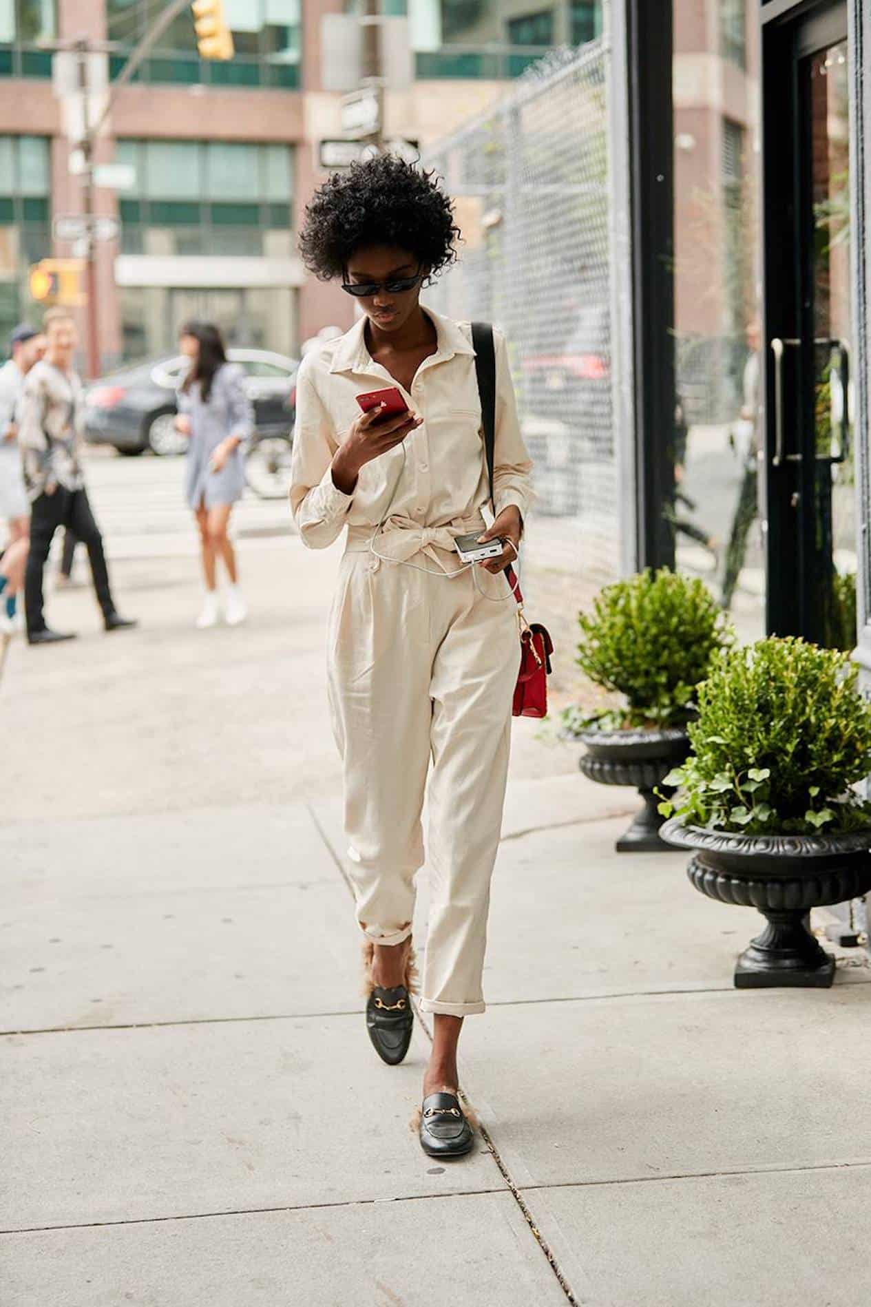 image of a black woman walking down the sidewalk wearing a white jumpsuit and Gucci mules