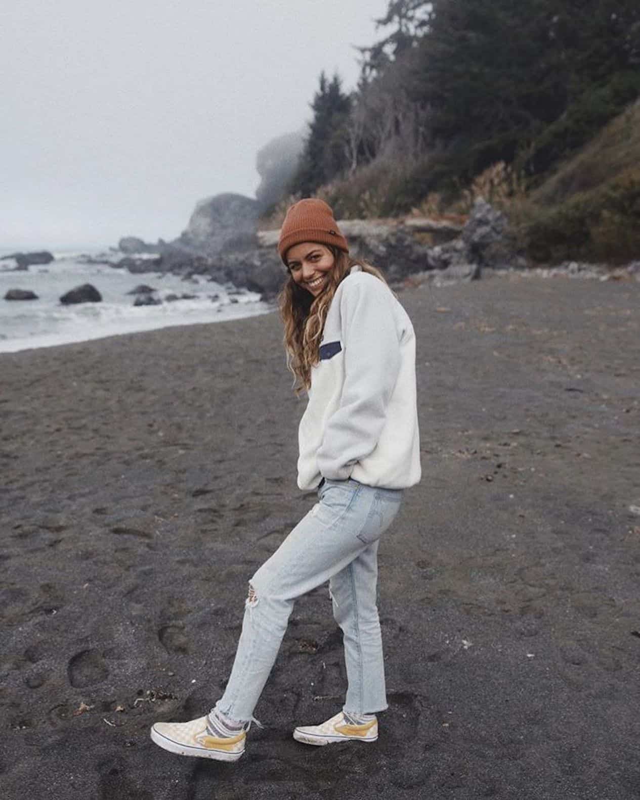 Woman wearing light wash jeans, white pullover and Vans on the beach.