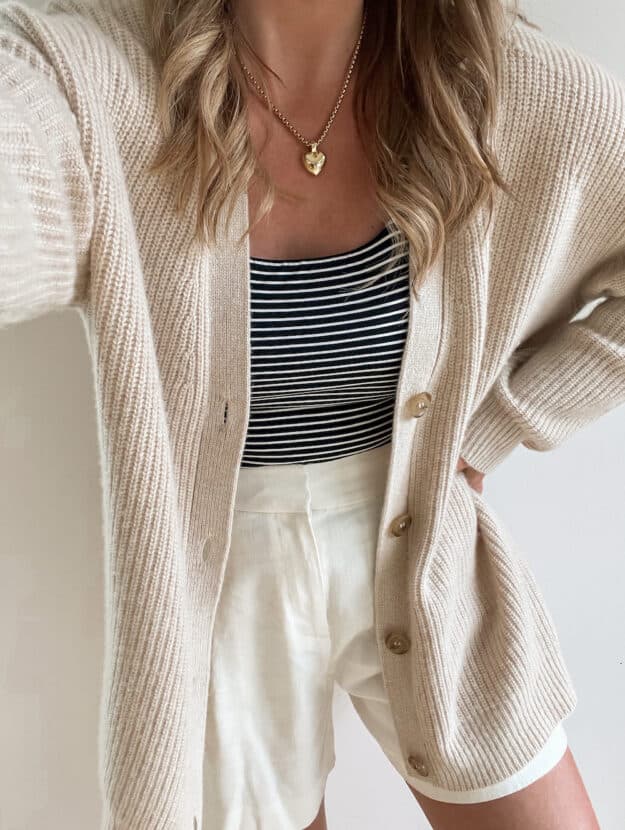 woman wearing a Jenni Kayne cashmere cocoon cardigan in oatmeal with a striped tank and ivory linen shorts