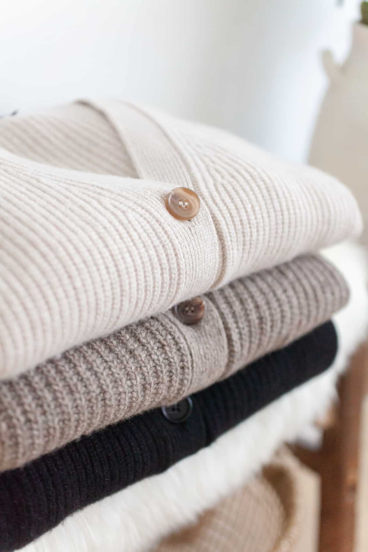 an up close image of three stacked knit cashmere cardigan sweaters in neutral colors