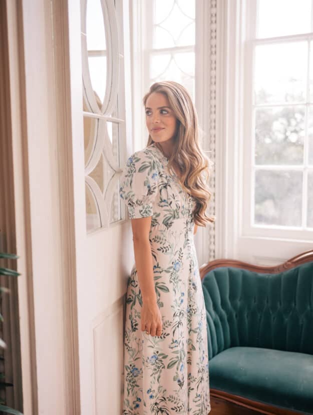a woman standing in a room with a green couch wearing a pretty floral dress