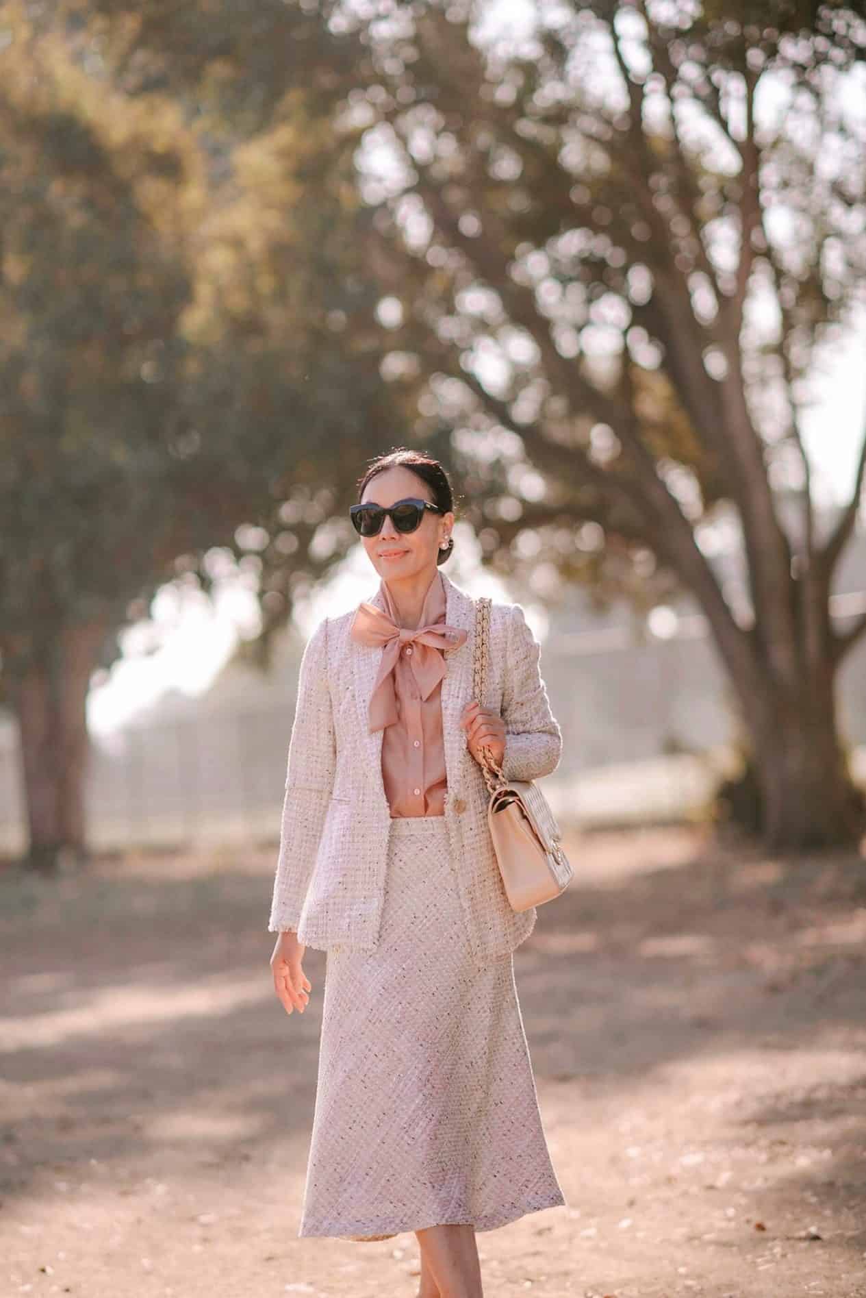 image of a woman in a pink tweed skirt suit walking down a road with trees in the background