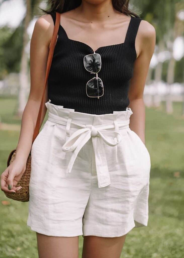 image of a woman from the shoulders down wearing a black tank top and white paperbag shorts