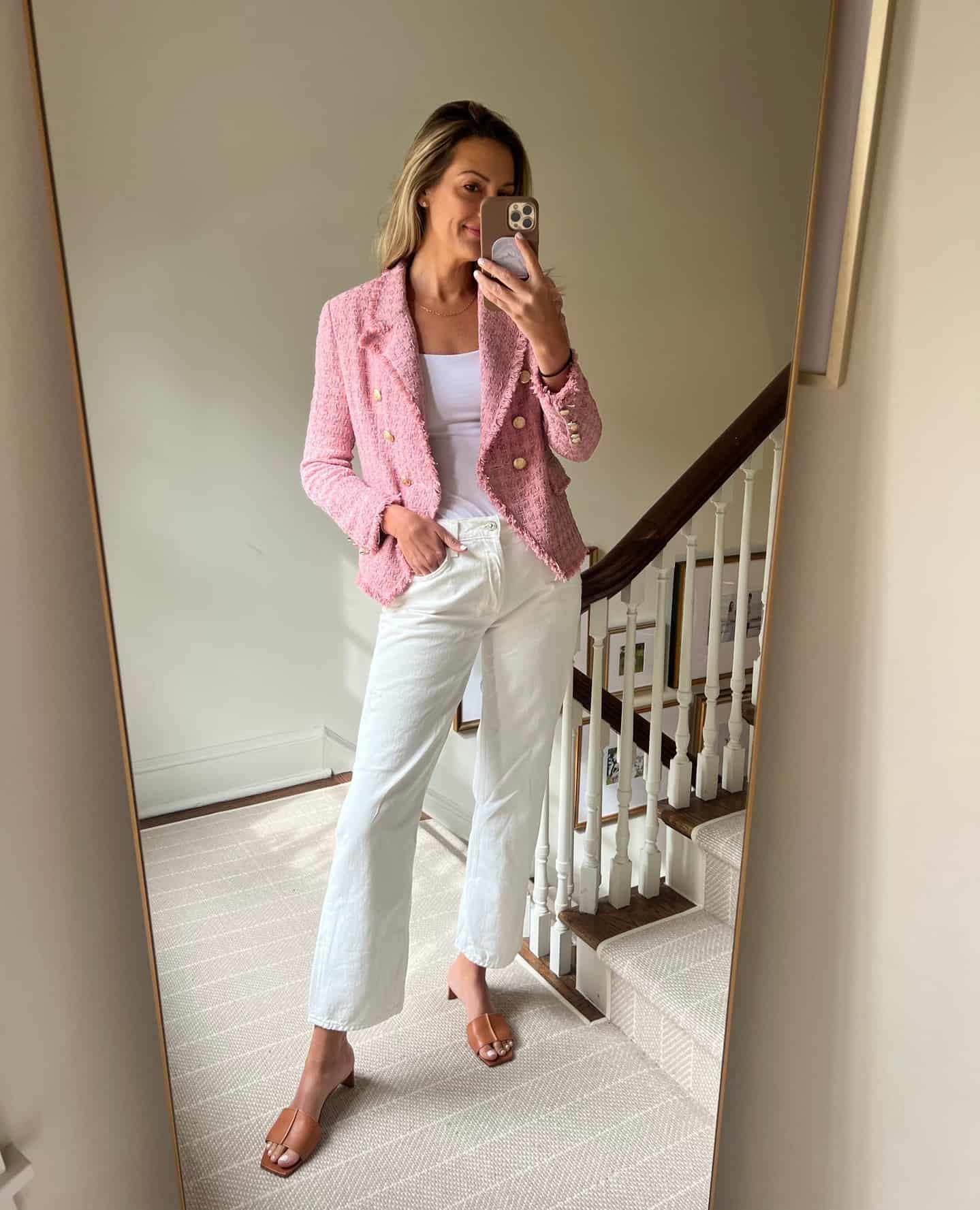 Woman wearing a country club attire outfit with a pink tweed jacket, white jeans, and brown sandals