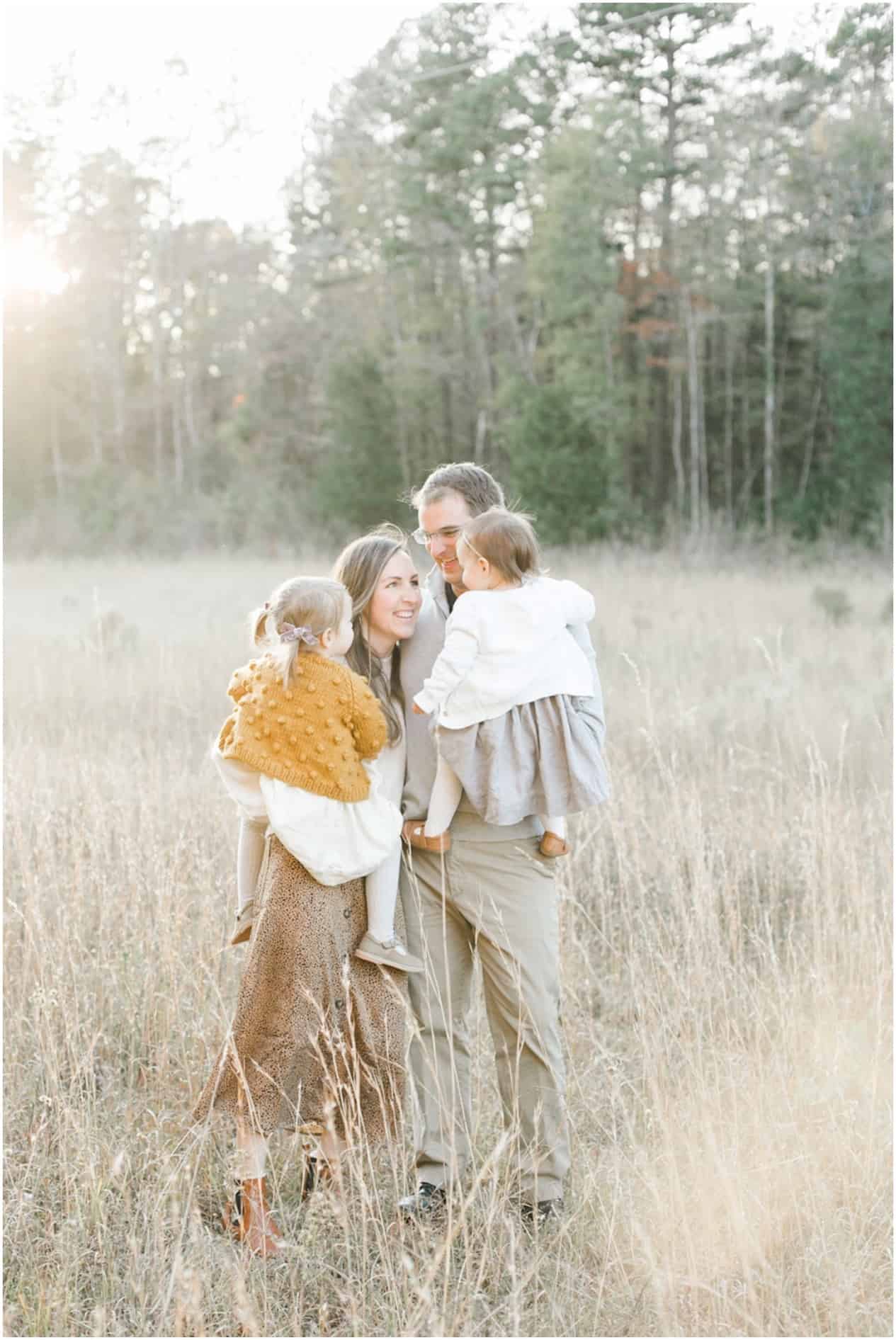 image of a family of four standing in a grassy field wearing neutral colors