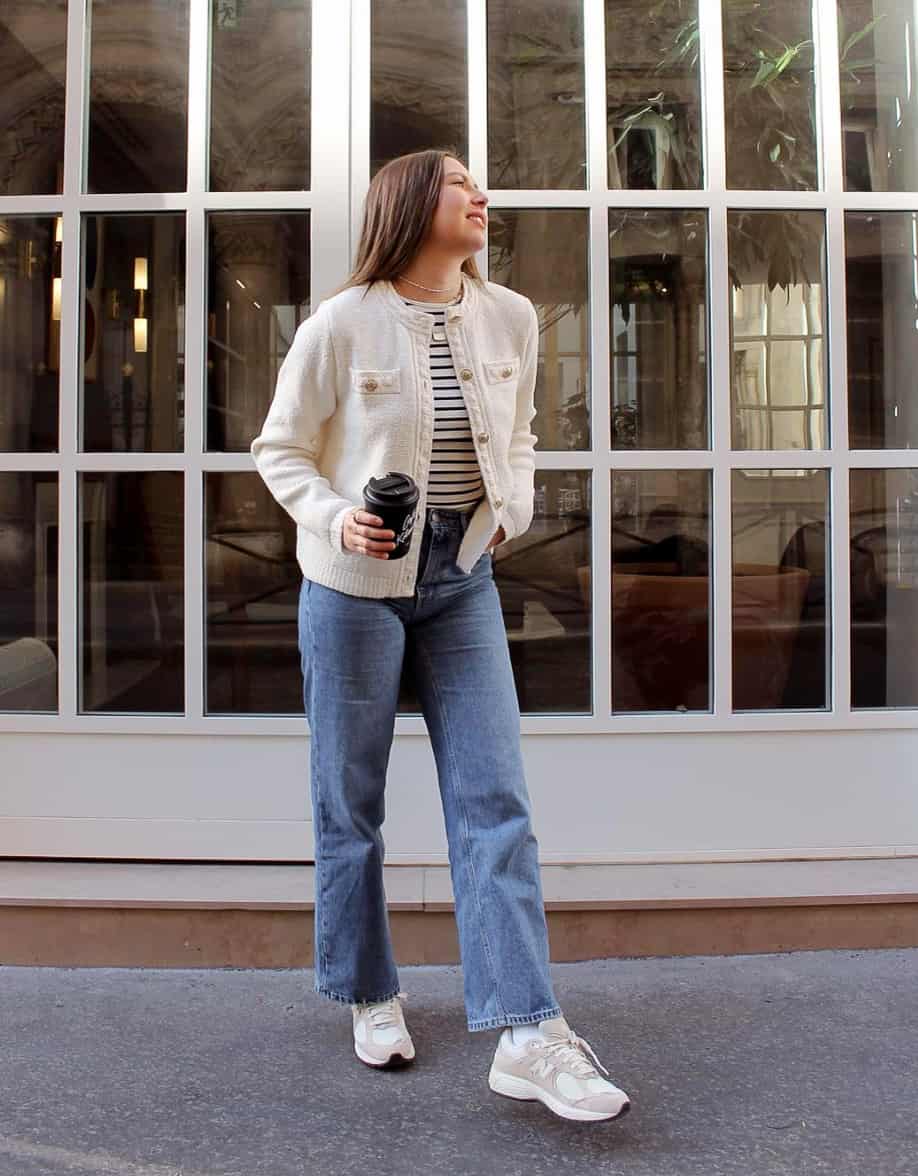 Woman wearing a cropped tweed white jacket over a striped shirt with straight leg jeans and sneakers