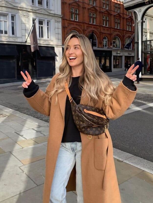 image of a woman with long blonde hair wearing a brown camel coat, Louis Vuitton bumbag, and jeans