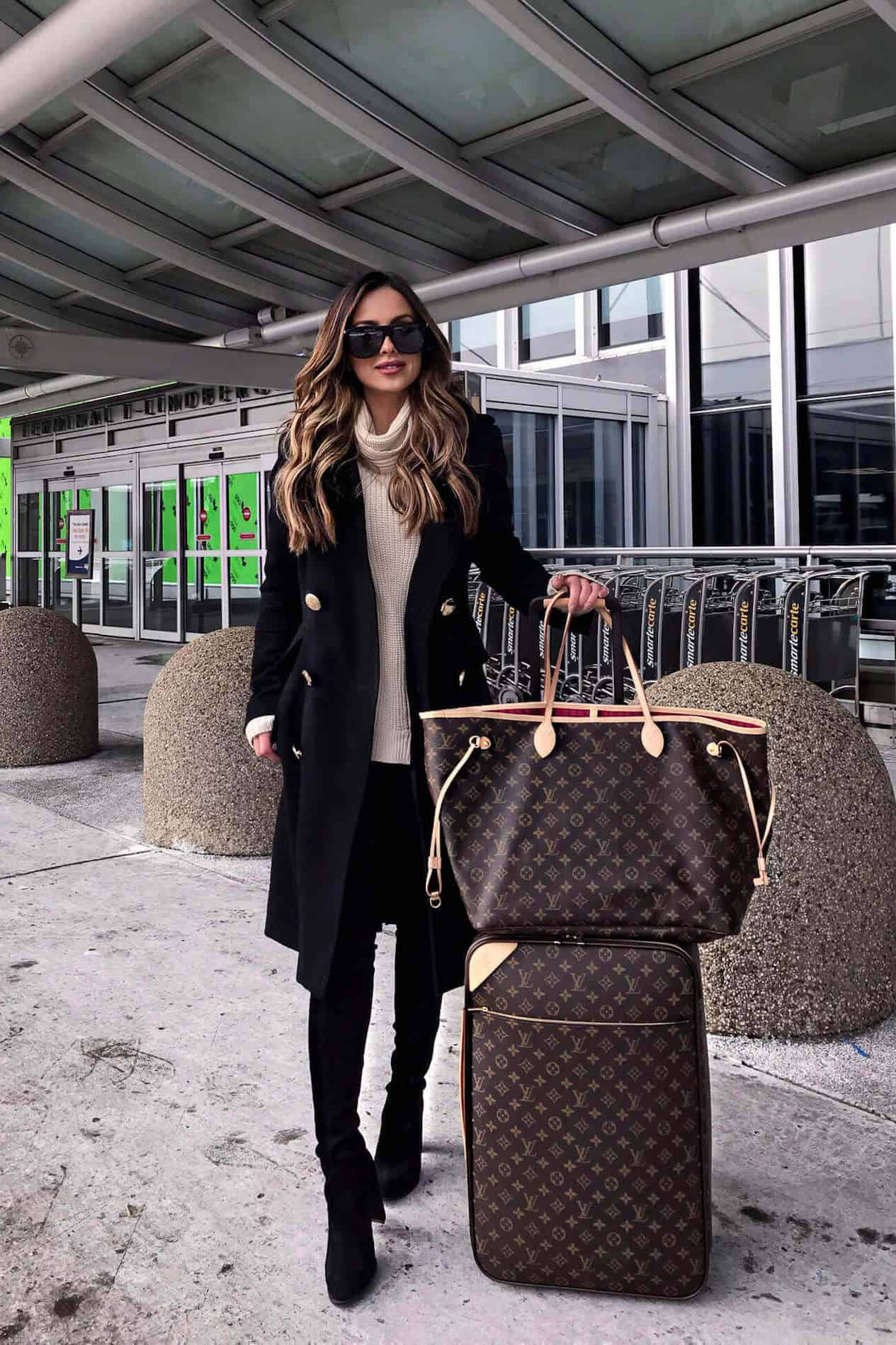 image of a woman with long brown hair standing outside an airport terminal with Louis Vuitton luggage