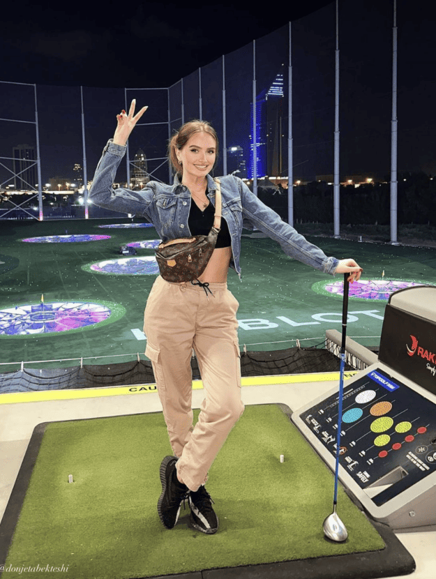 woman at Top Golf wearing a denim jacket over a black crop top with tan cargo pants and black sneakers