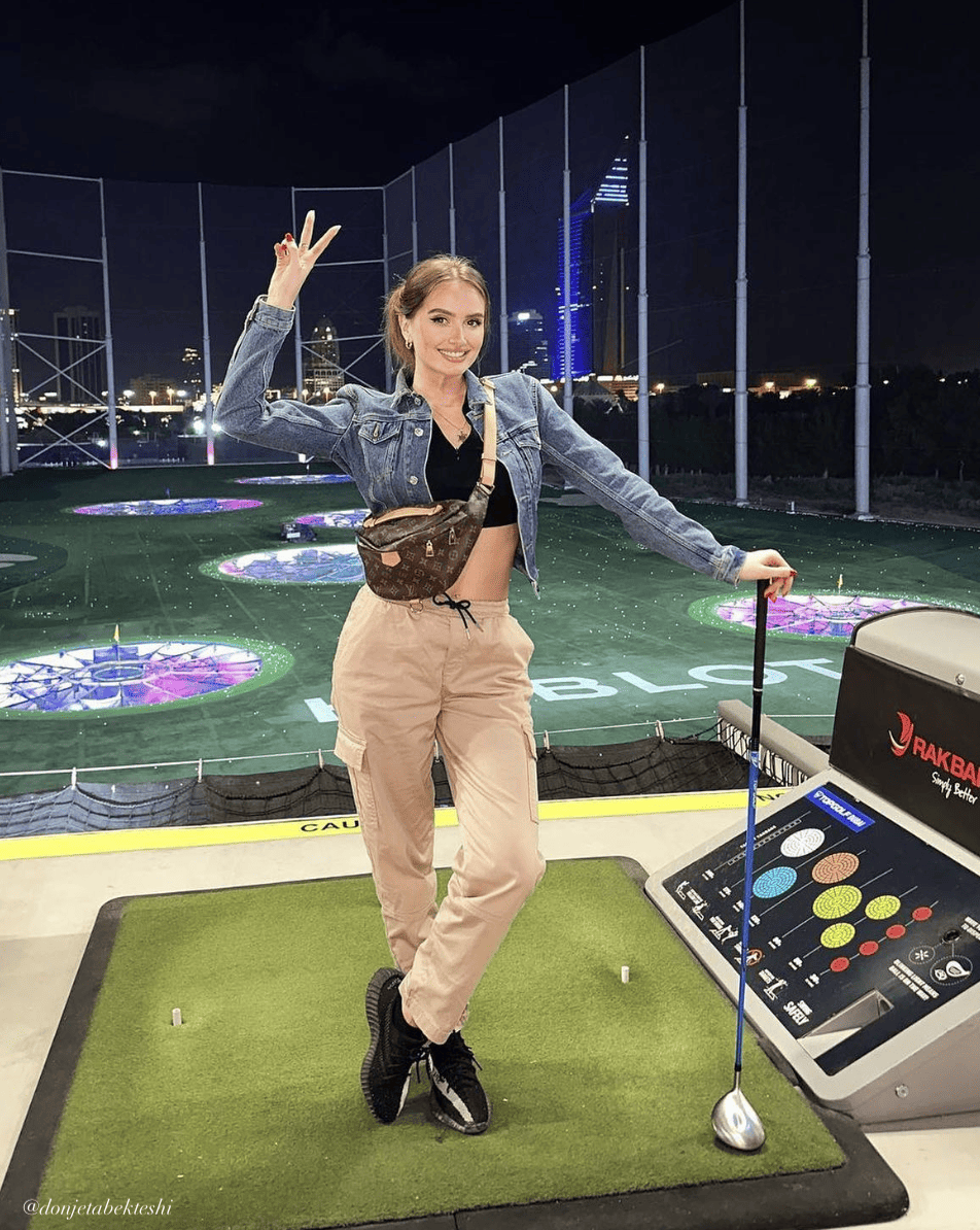 woman at Top Golf wearing a denim jacket over a black crop top with tan cargo pants and black sneakers