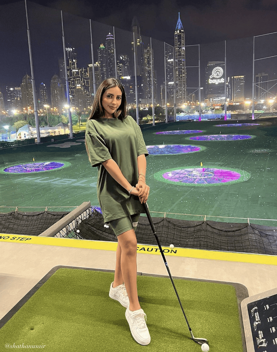 woman at Top Golf wearing an oversized green t-shirt with green biker shorts and sneakers