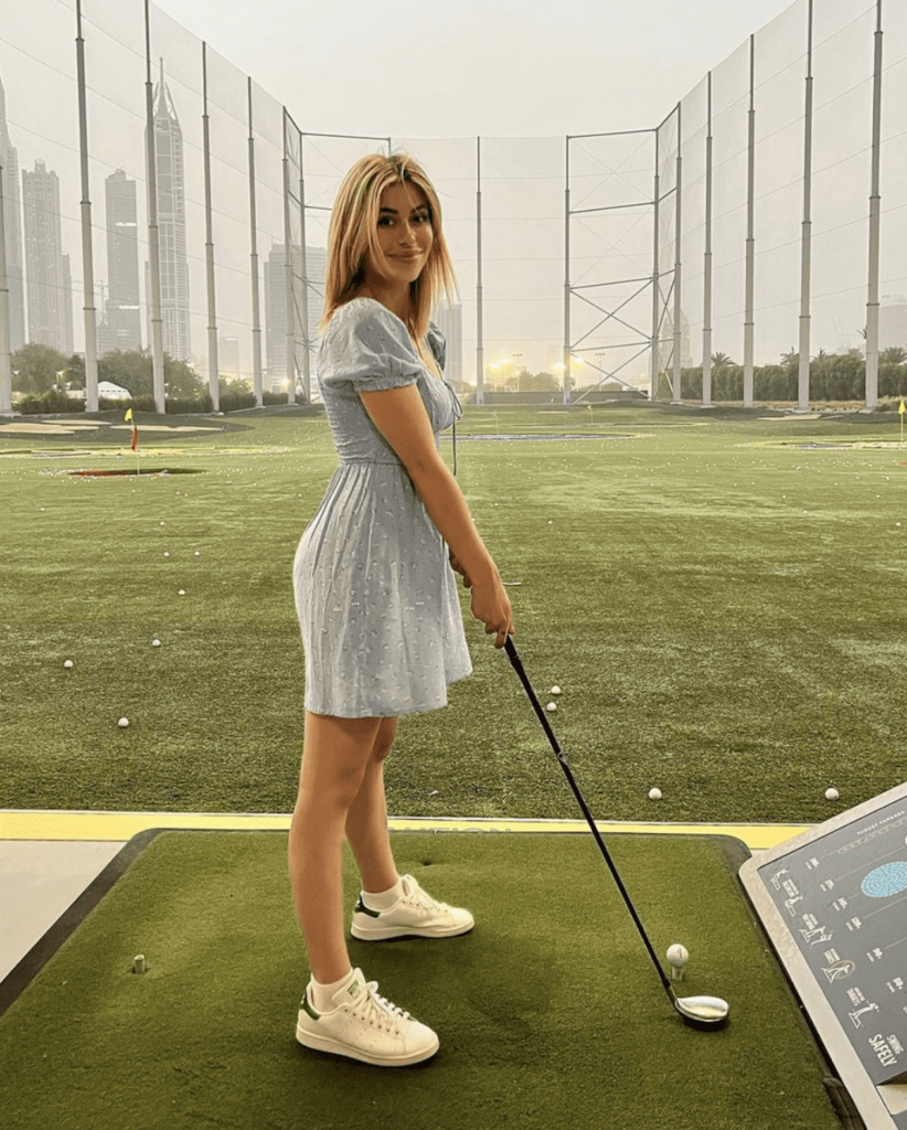 image of a woman playing golf at Topgolf wearing a blue floral mini dress and white sneakers