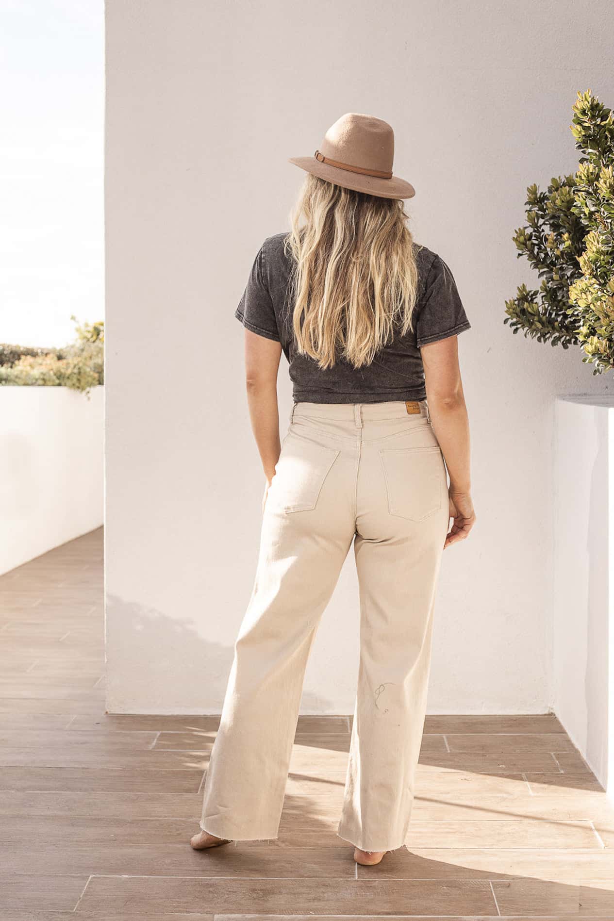 image of a woman with long blonde hair from the back wearing white wide leg jeans, a dark t-shirt, and a hat