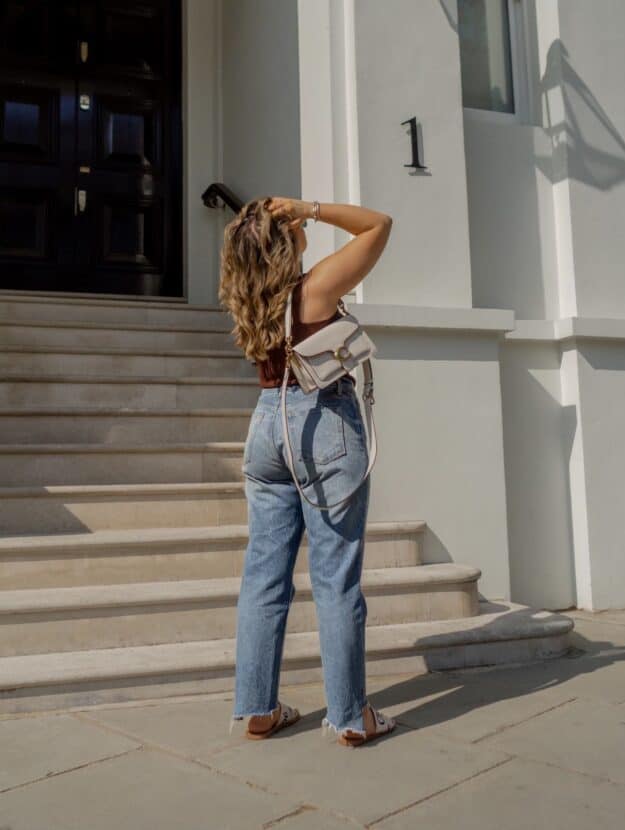 image of a curvy woman standing in front of a set of steps from behind wearing jeans and a tank top