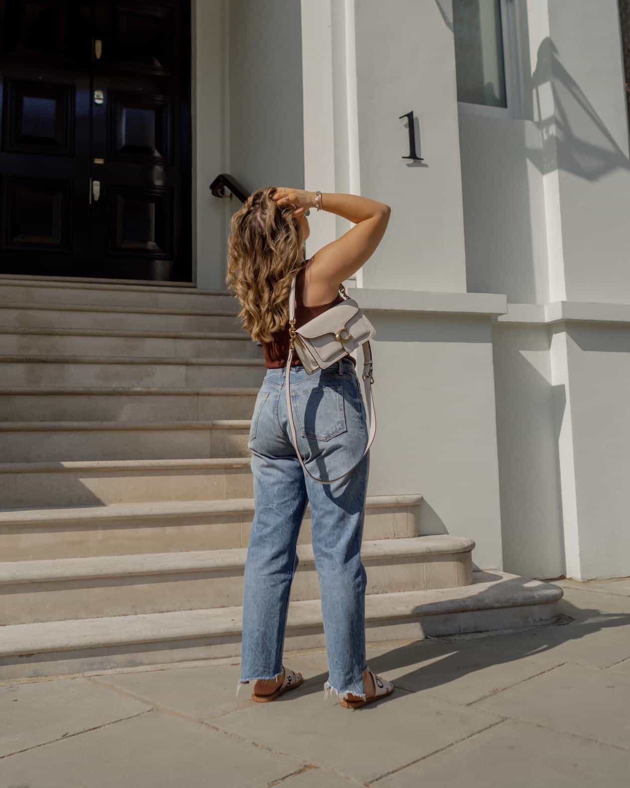 image of a curvy woman standing in front of a set of steps from behind wearing jeans and a tank top 