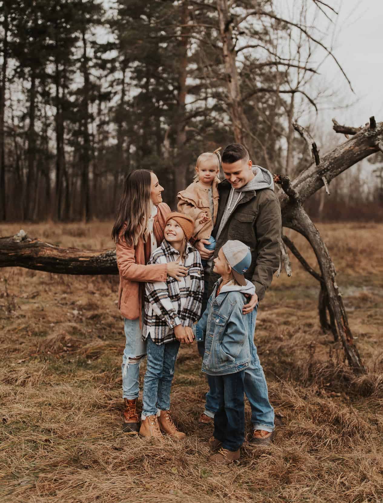 image of a family of five standing in a wooded area in the fall wearing casual jackets and jeans