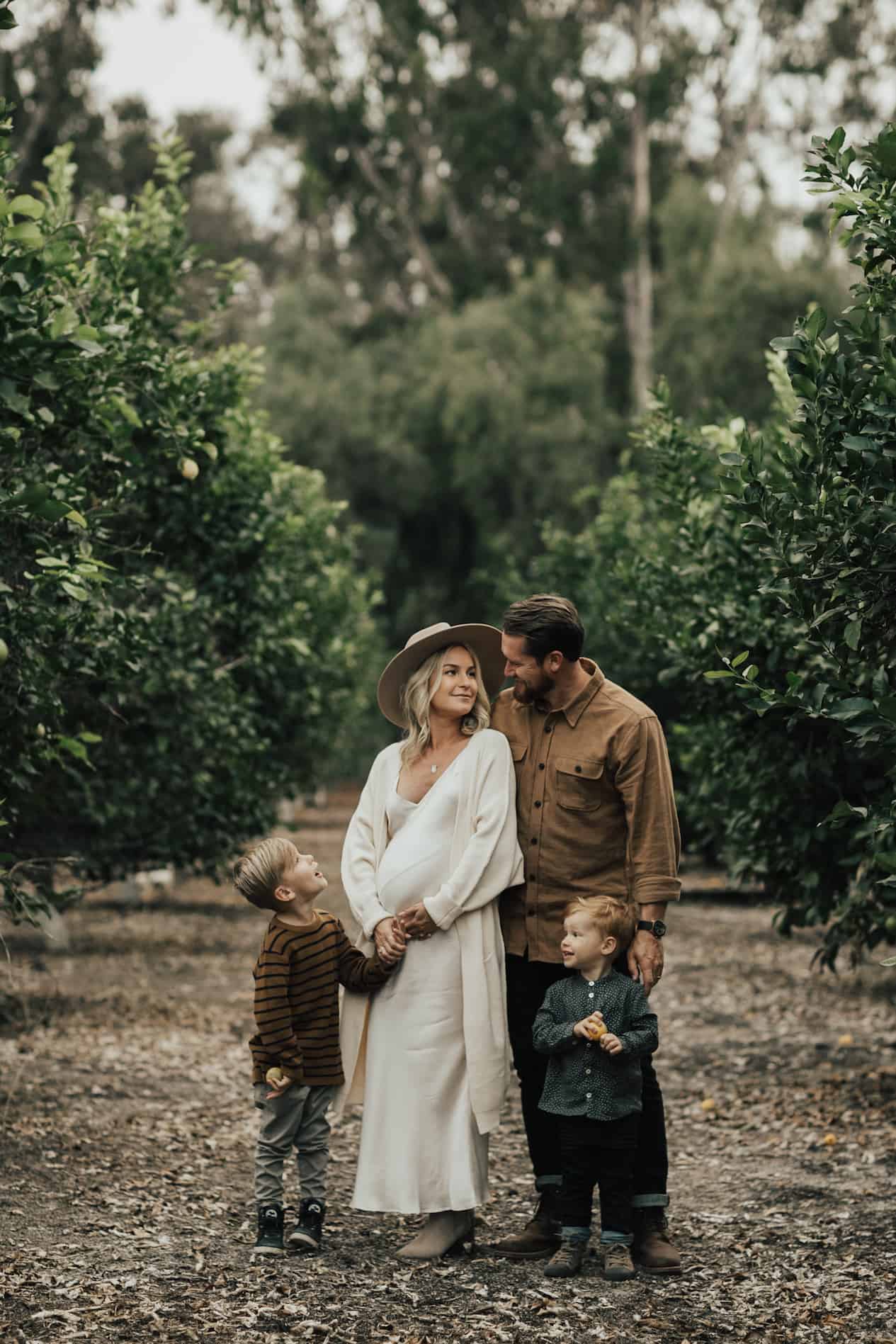 image of a family standing in a treed area wearing neutral colors for a family photoshoot
