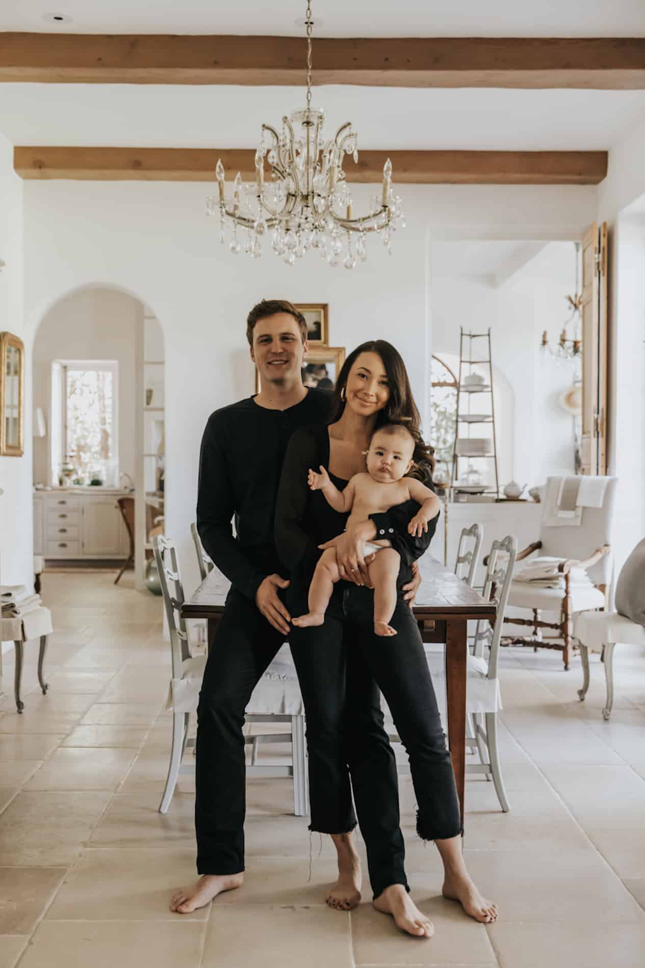 image of a woman and man wearing all black outfits sitting casually in their home holding a baby in a diaper in their arms