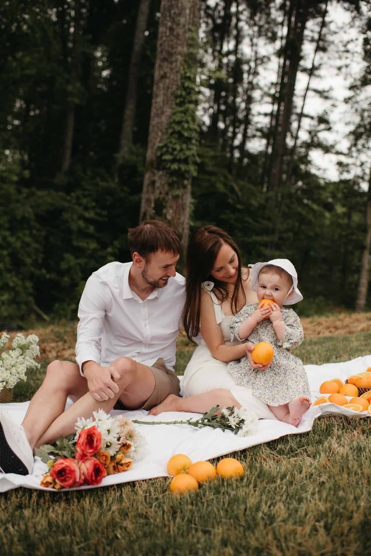 image of a small family having a picnic in the summer, wearing neutral color tones and eating oranges