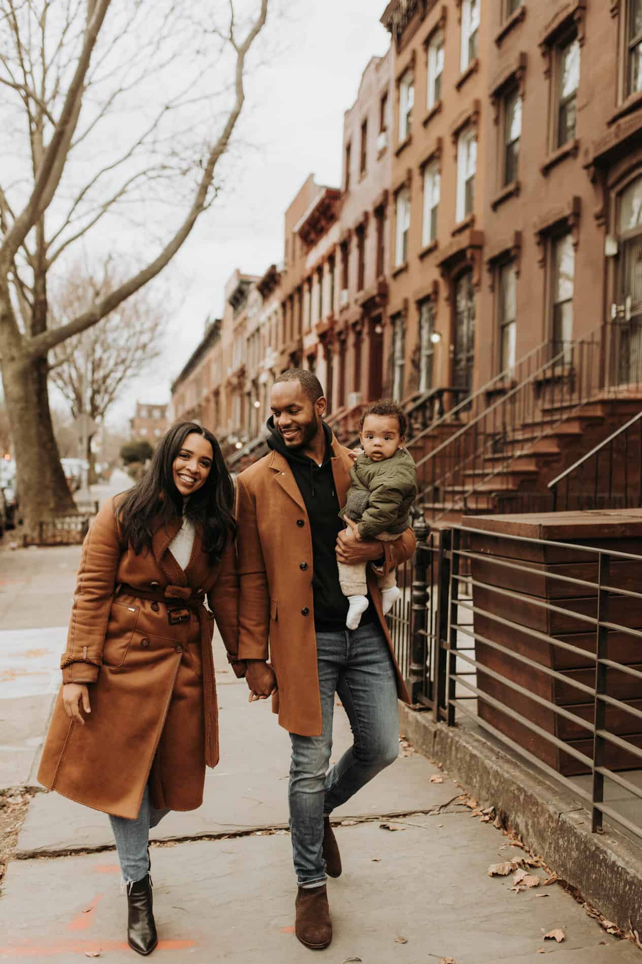image of a black family walking down the street with a mom, dad, and baby wearing rust brown matching jackets and denim