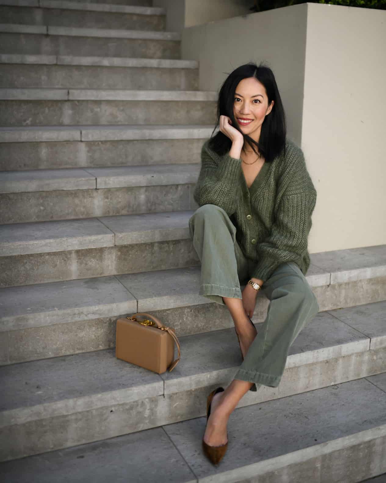 image of a woman sitting on set of stairs wearing a green cardigan, green pants, and brown suede heels