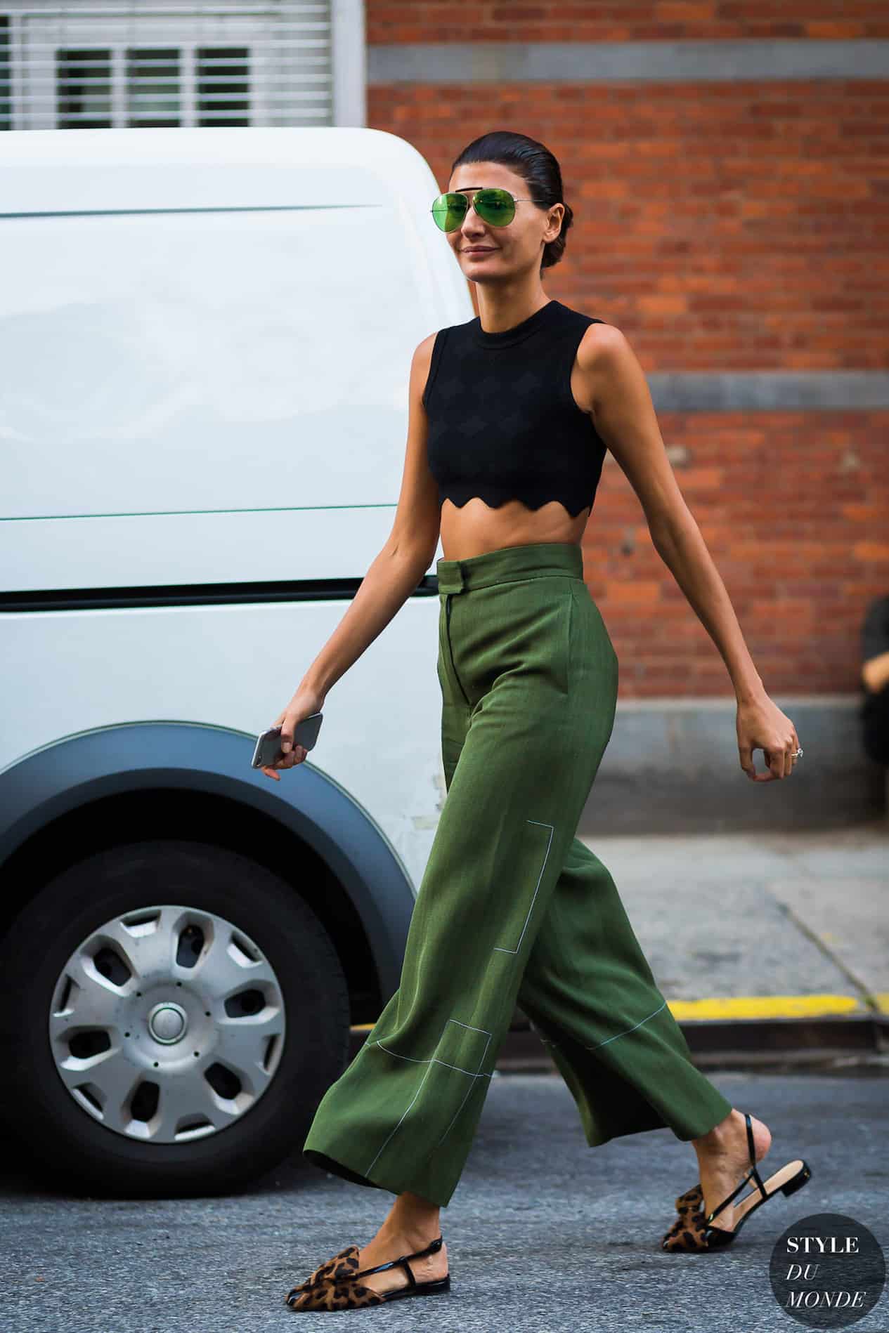 image of a woman walking down the road wearing wide leg green pants, a black crop top, and pointy leopard mules