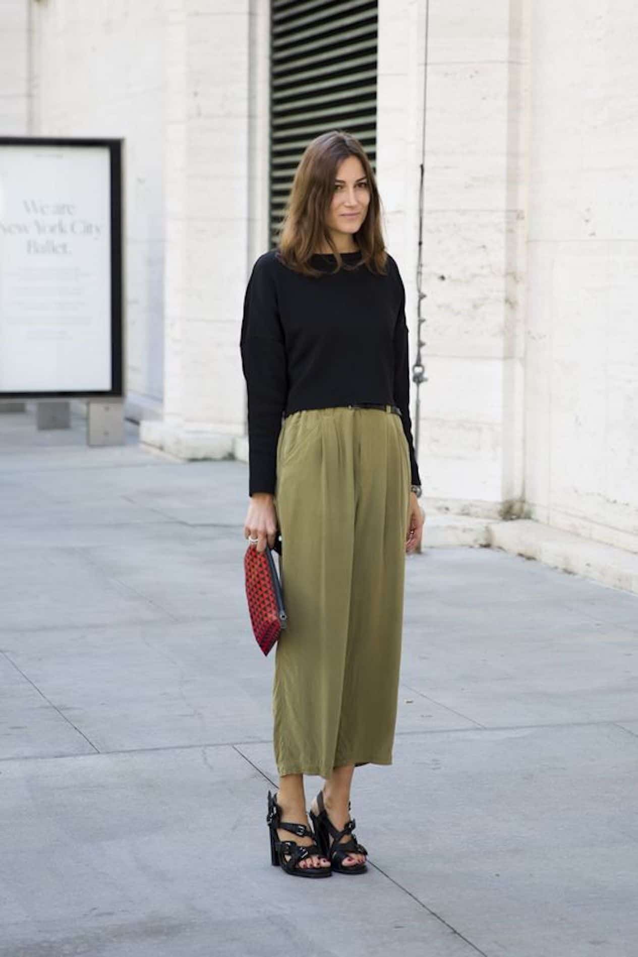 image of a woman standing on a sidewalk wearing green flowy pants, a black sweater, and black sandal heels