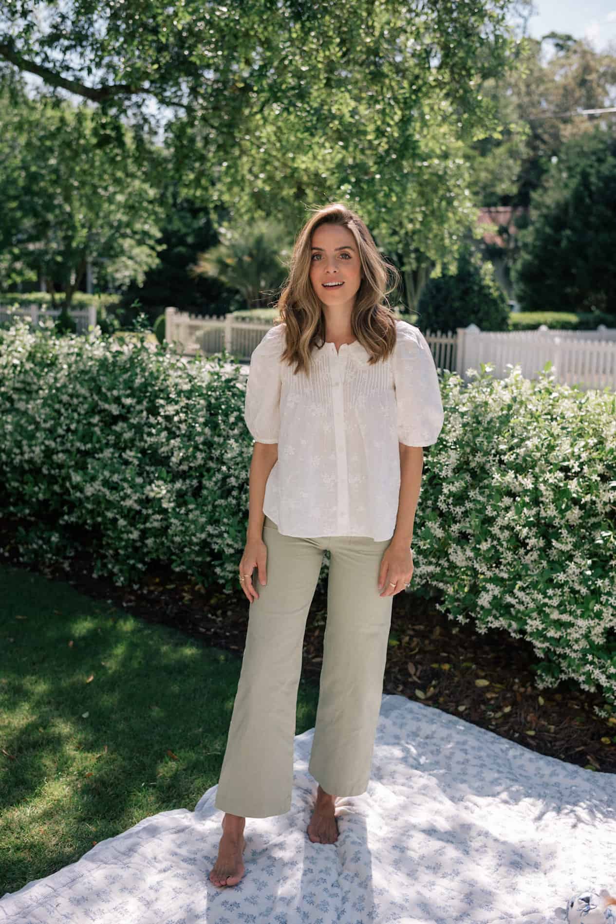 image of a woman wearing a white embroidered blouse and light green pants standing in a treed area