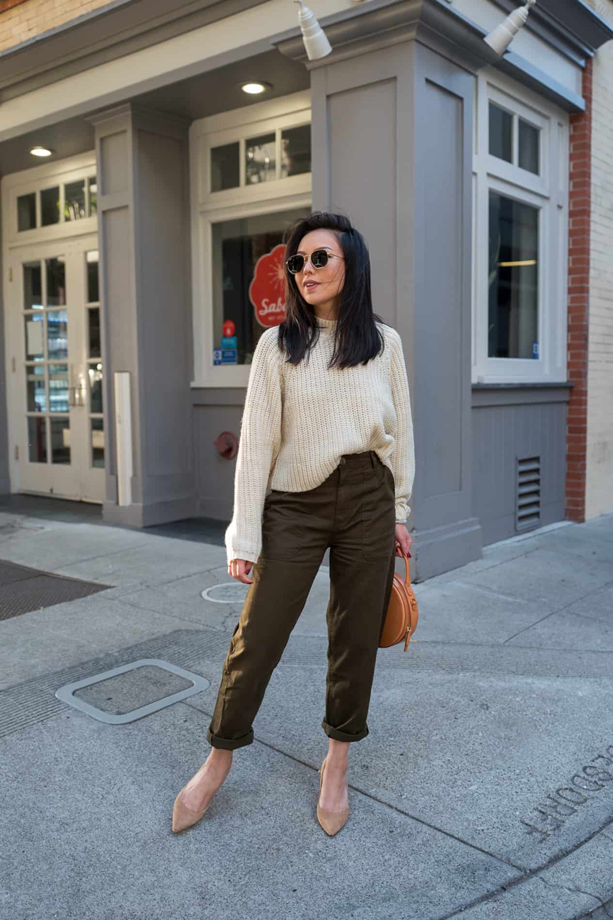 image of a woman standing on a sidewalk wearing a knit ivory sweater, green cargo pants, and a pair of nude heels