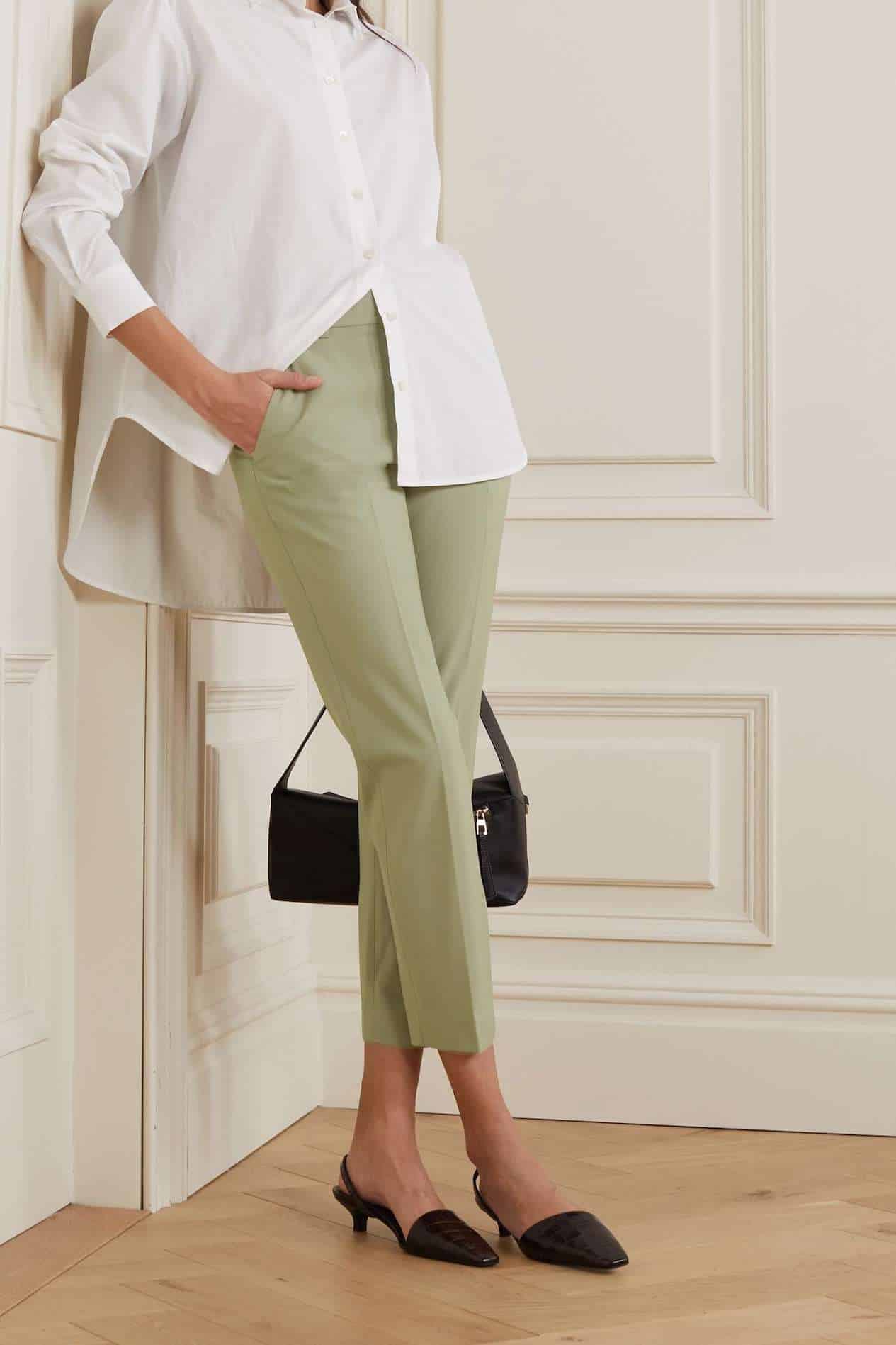 image of a woman from the neck down wearing a white button up shirt, light green pants, black pointy mules, and a black purse