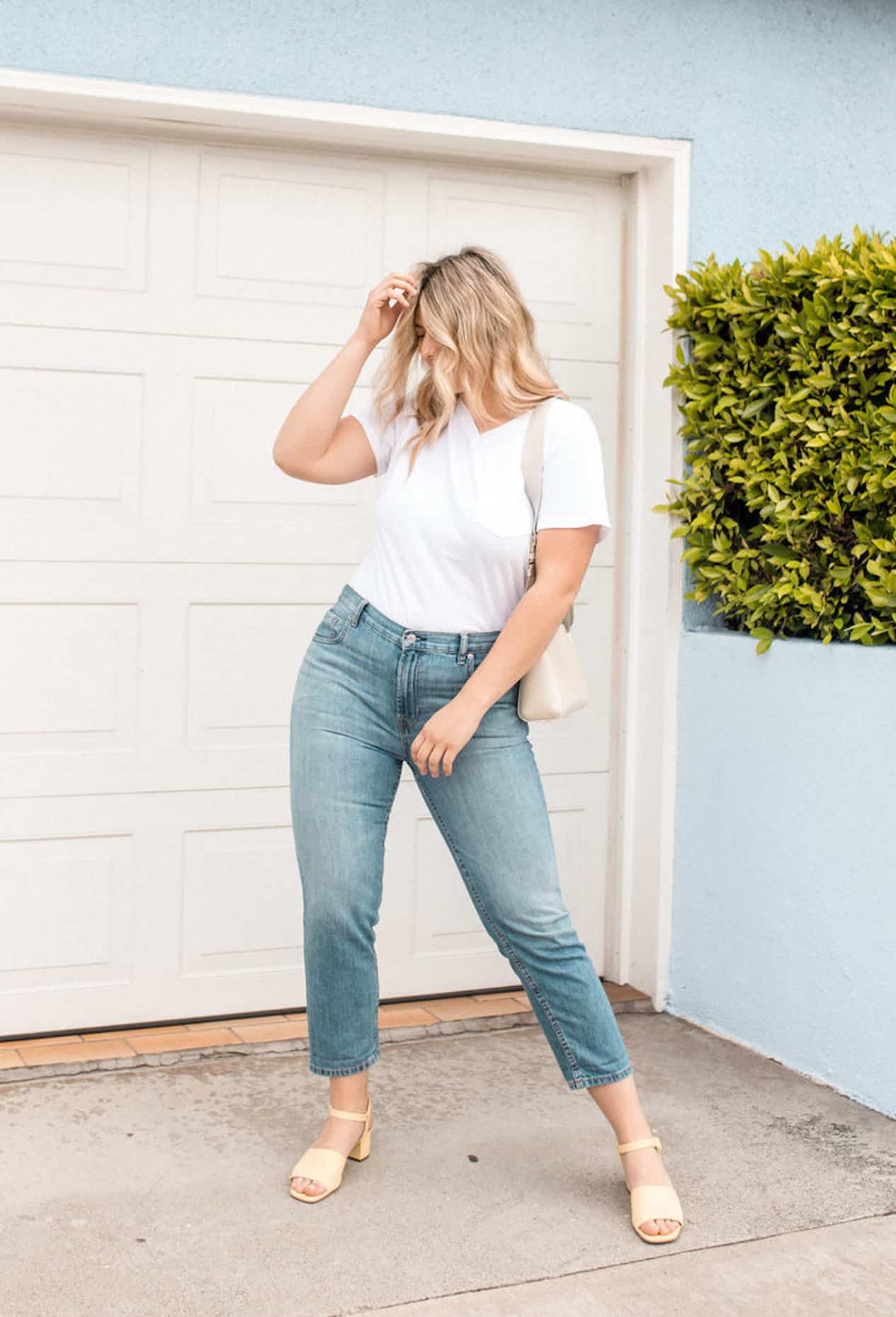 image of a curvy blonde woman wearing a white t-shirt, blue jeans, and sandals standing in front of a white garage door