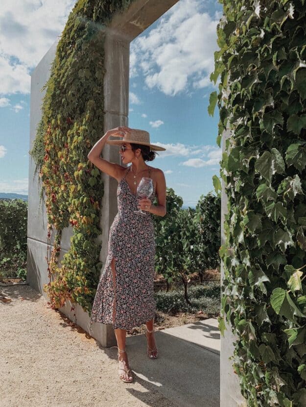 image of a woman in a floral midi dress with a sun hat holding a glass of wine at a winery