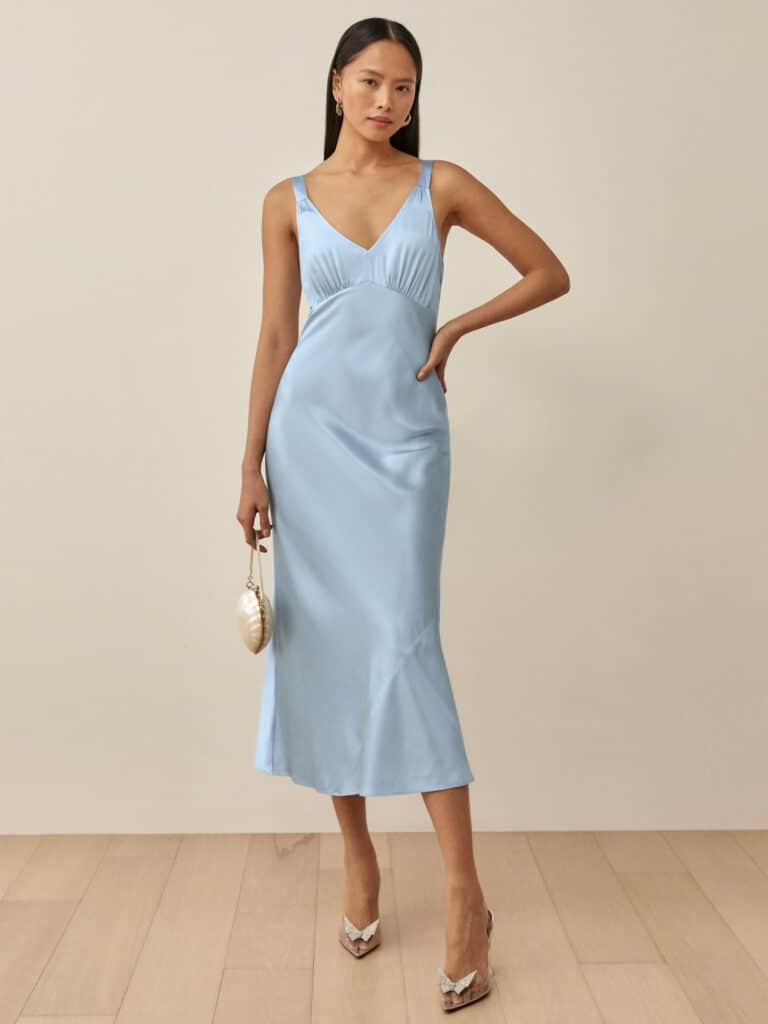 image of a woman in a light blue silk midi slip dress with a shell purse and clear heels