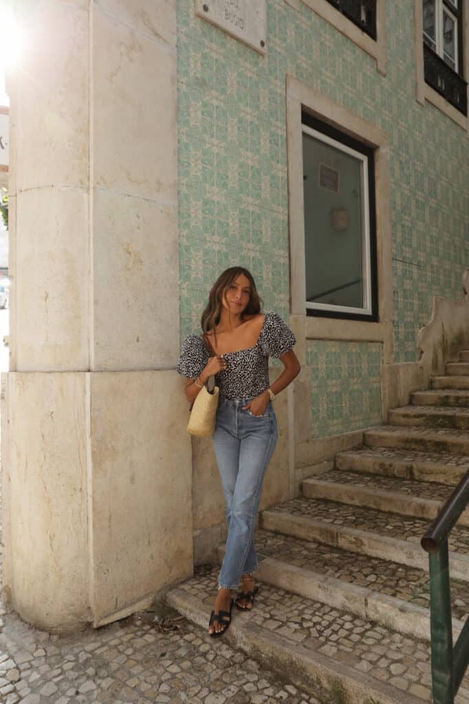 image of a woman standing on a set of stairs wearing a pretty blouse, jeans, and sandals