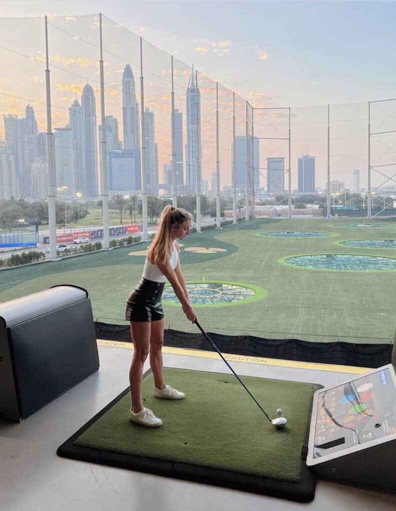 image of a woman playing gift at Topgolf wearing black leather shorts and a white tank top with sneakers