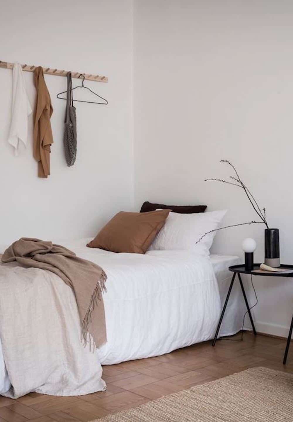 image of a small bed in a room with white sheets and neutral accents, and a wood peg board on the wall