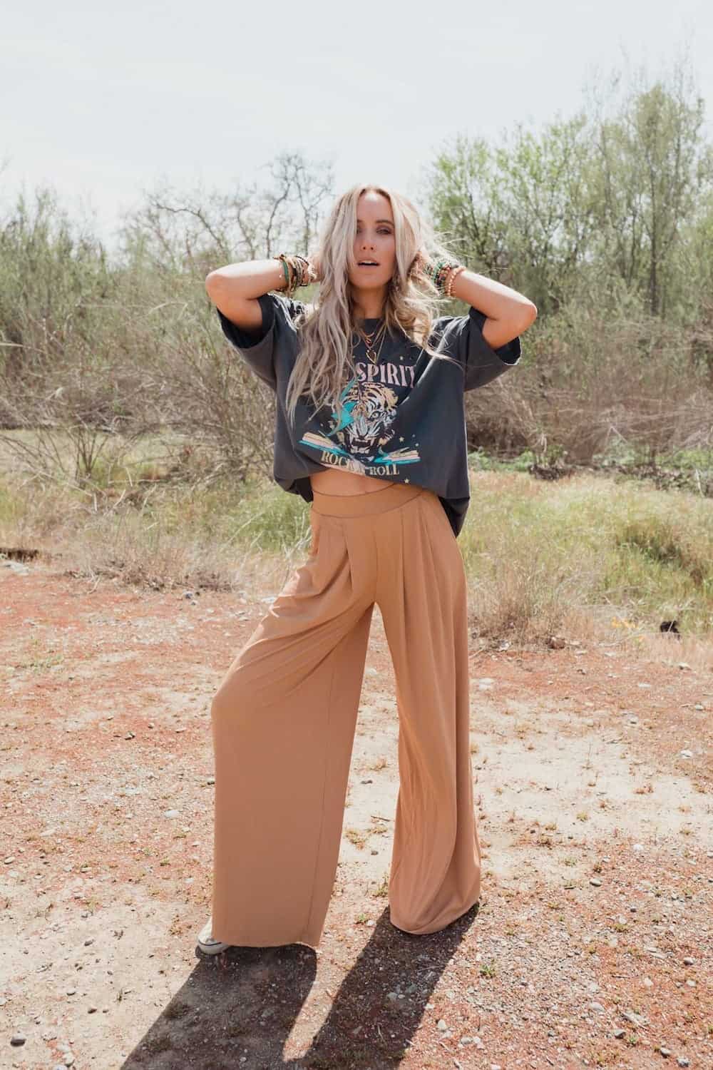 image of a blonde woman wearing wide leg tan pants and a graphic t-shirt in a grassy area