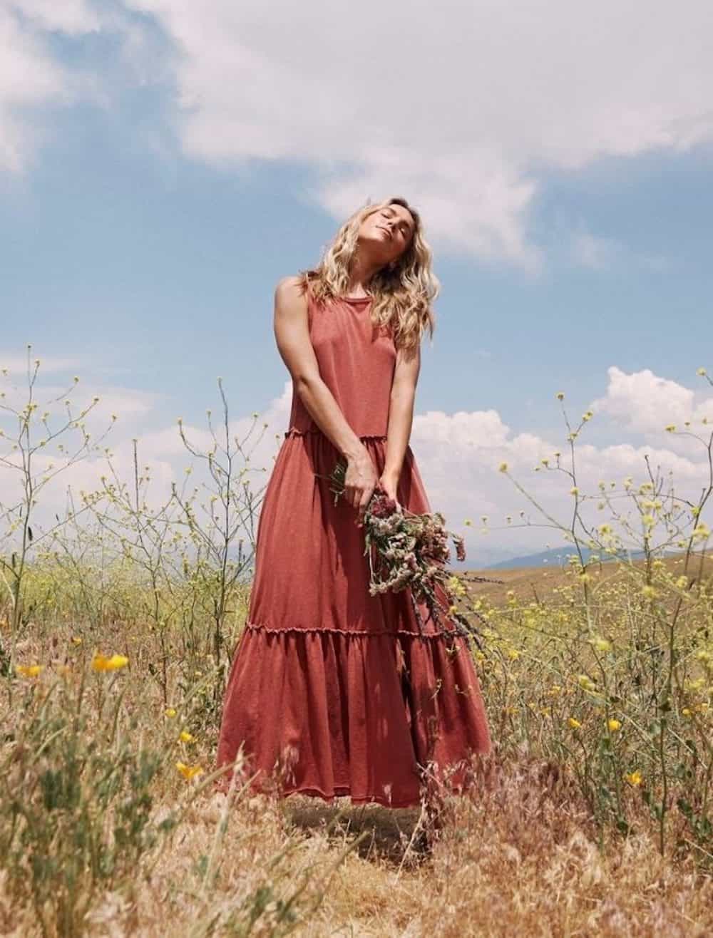 image of a woman standing in a field holding flowers wearing a pink maxi dress