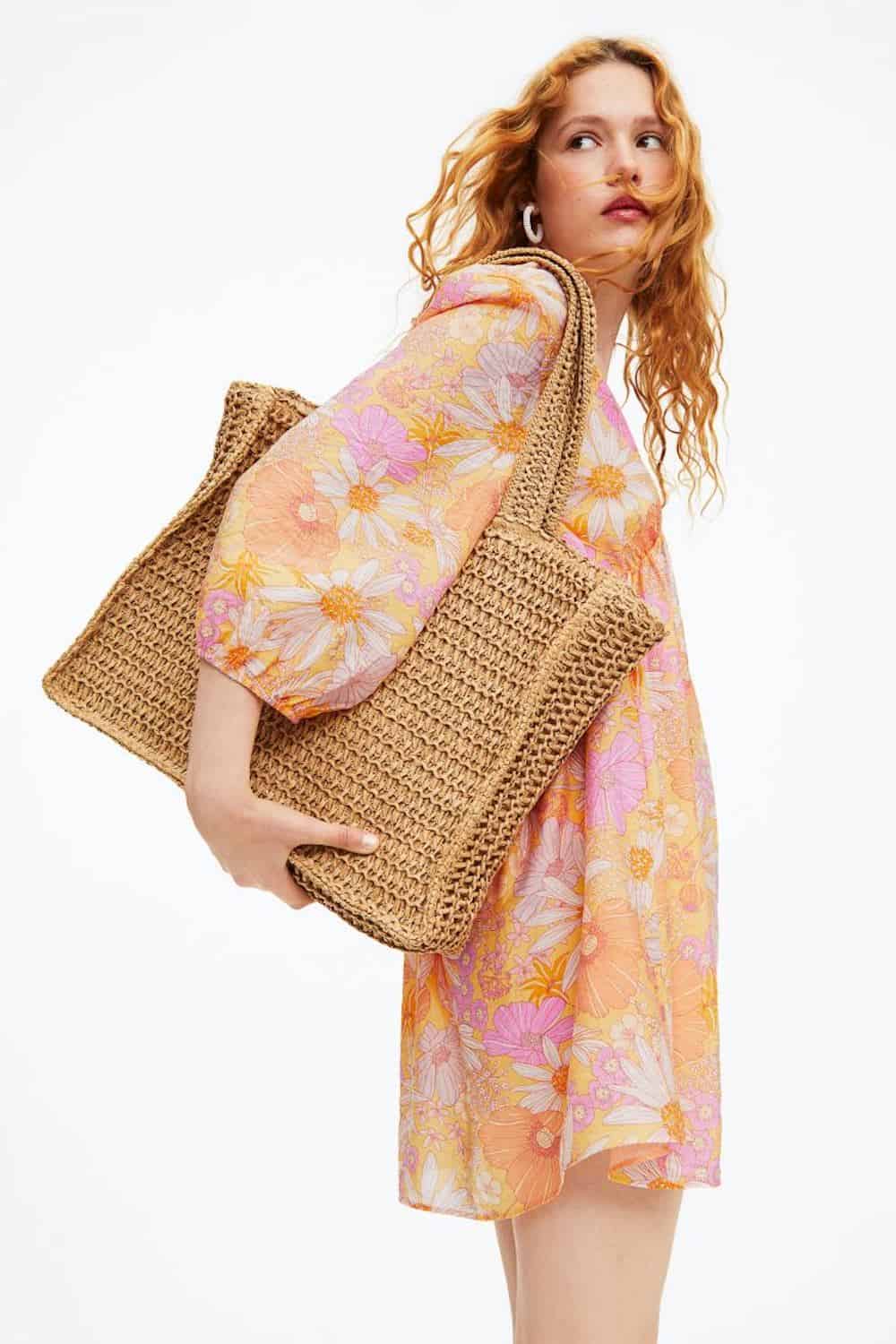 image of a woman in a floral mini dress holding a large woven straw bag