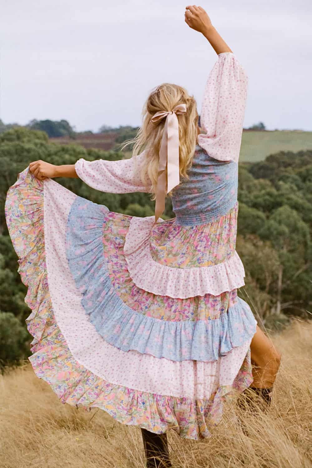 image of a woman from the back wearing a colourful floral tiered dress and she's dancing in a field