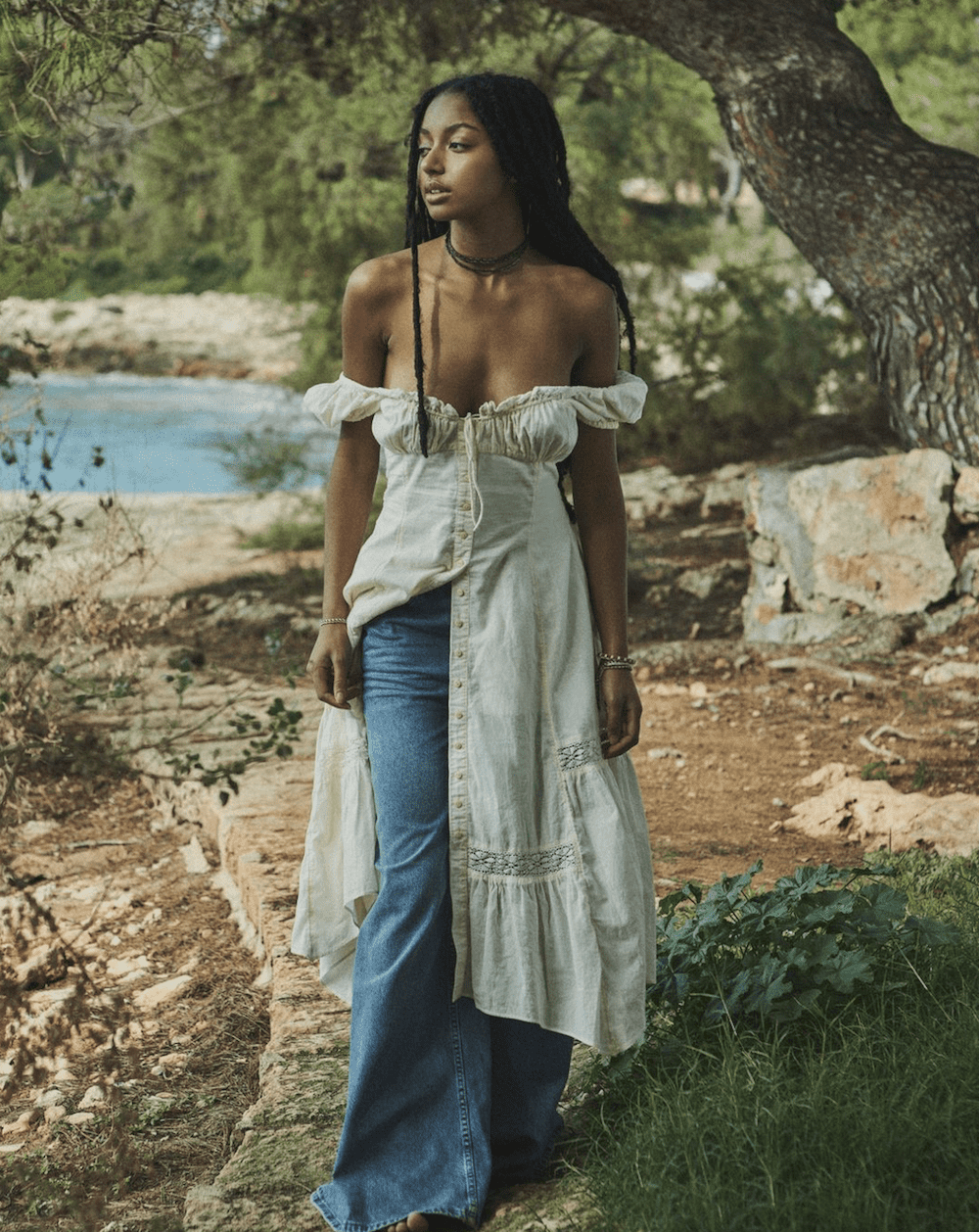 image of a beautiful black woman in a boho style dress and flared jeans standing by the ocean
